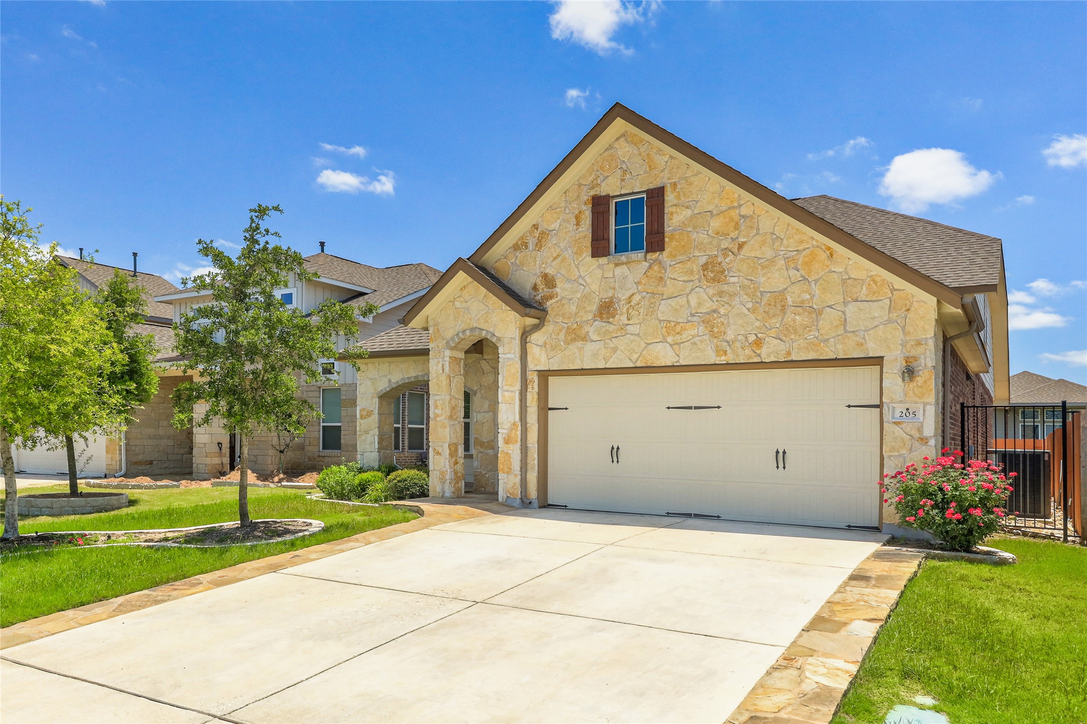 A stone-clad home with an attached garage, featuring a well-maintained front yard and a paved driveway.