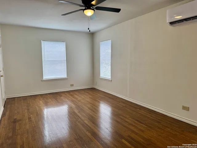 an empty room with wooden floor fan and windows