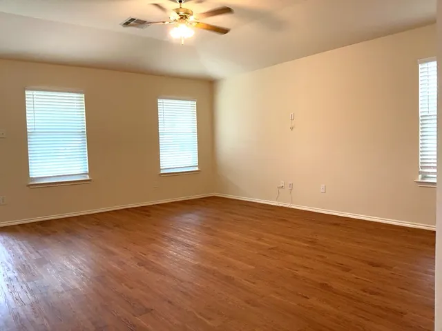 an empty room with wooden floor fan and windows
