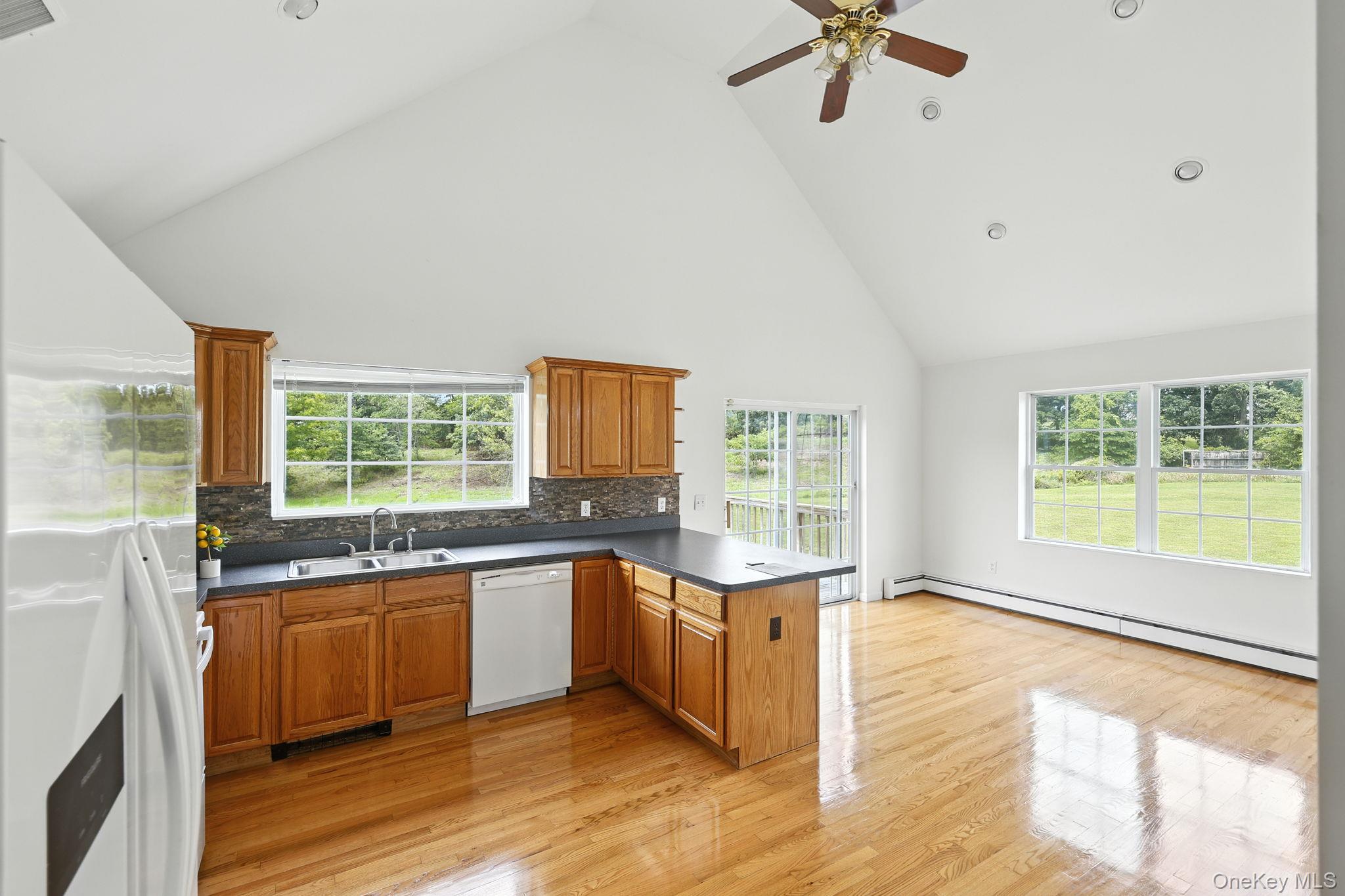 160 Pirog Road Pine Bush, NY 12566 - Photo 5 of 26 Kitchen with brown cabinetry, high vaulted ceiling, a peninsula, white appliances, and dark countertops