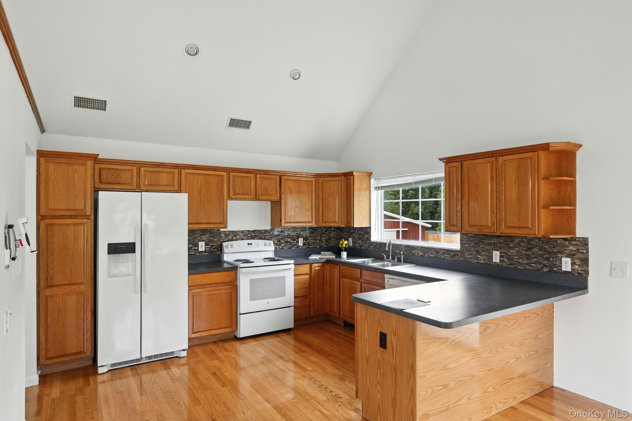 160 Pirog Road Pine Bush, NY 12566 - Photo 6 of 26 Kitchen featuring brown cabinets, white appliances, dark countertops, high vaulted ceiling, and a peninsula