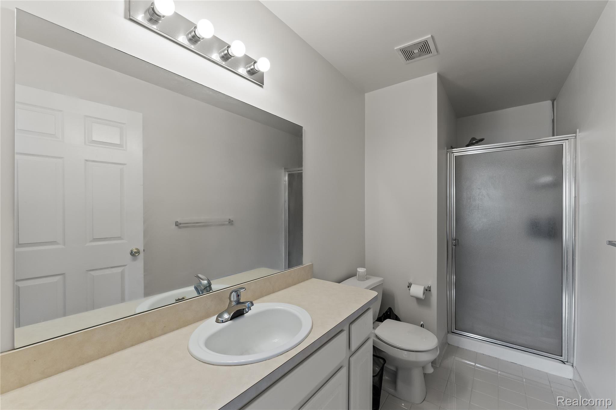 1861 Flagstone Circle Rochester, MI 48307 - Photo 17 of 21 Bathroom featuring a vanity with an integrated sink, a large wall-mounted mirror, a four-bulb vanity light, a glass-enclosed shower, and a white toilet