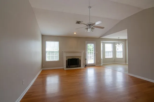 an empty room with wooden floor fireplace and windows
