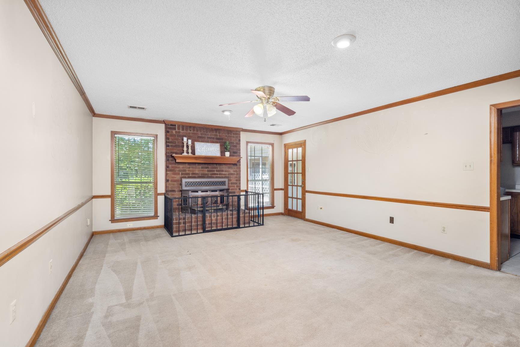5015 Eagles Nest Lane Bartlett, TN 38002 - Photo 17 of 39 Unfurnished living room with a ceiling fan, ornamental molding, a brick fireplace, a textured ceiling, and light colored carpet