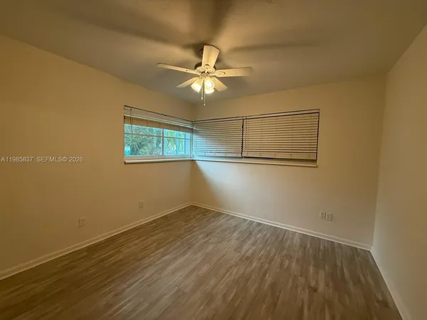 an empty room with wooden floor fan and windows