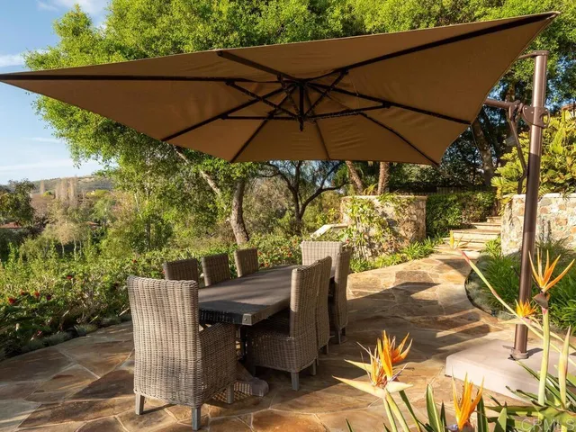 a view of a patio with table and chairs under an umbrella with large trees