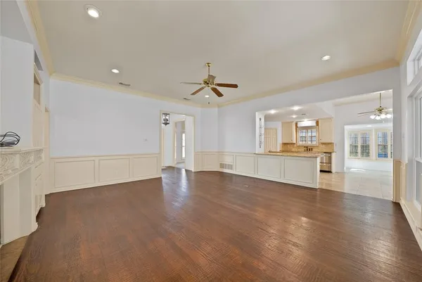 a view of an empty room with wooden floor and a kitchen