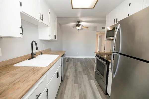 a kitchen with stainless steel appliances a refrigerator a sink a stove and white cabinets