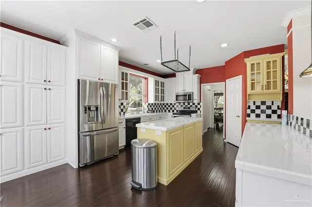 a kitchen with stainless steel appliances kitchen island granite countertop a stove a sink dishwasher and a refrigerator with wooden floor