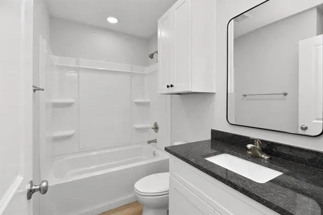 a bathroom with a granite countertop sink toilet mirror and bathtub