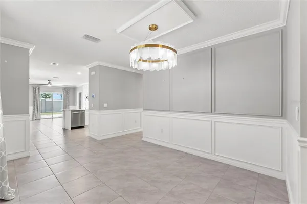 a view of an empty room with kitchen and chandelier fan