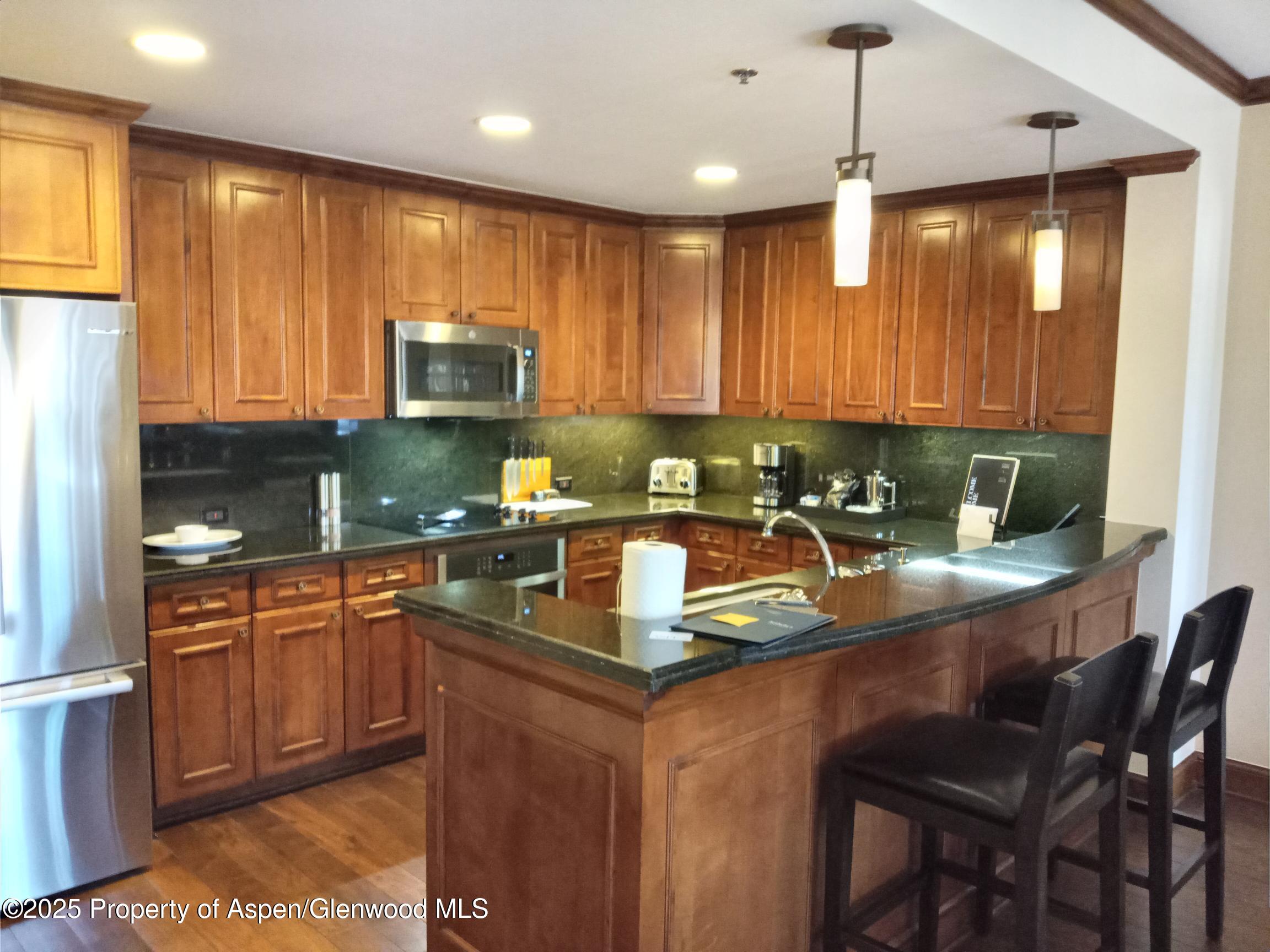 39 Boomerang Road, Unit 8209 SUMMER INTEREST 9 Aspen, CO 81611 - Photo 18 of 26 a kitchen with stainless steel appliances granite countertop wooden cabinets a refrigerator a sink a stove and island with wooden floor