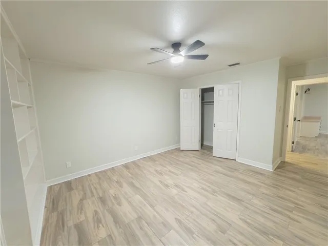 a view of an empty room with wooden floor and a ceiling fan