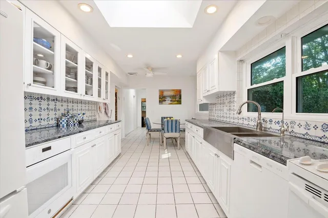a large white kitchen with granite countertop a sink and dishwasher a stove top oven with wooden floor