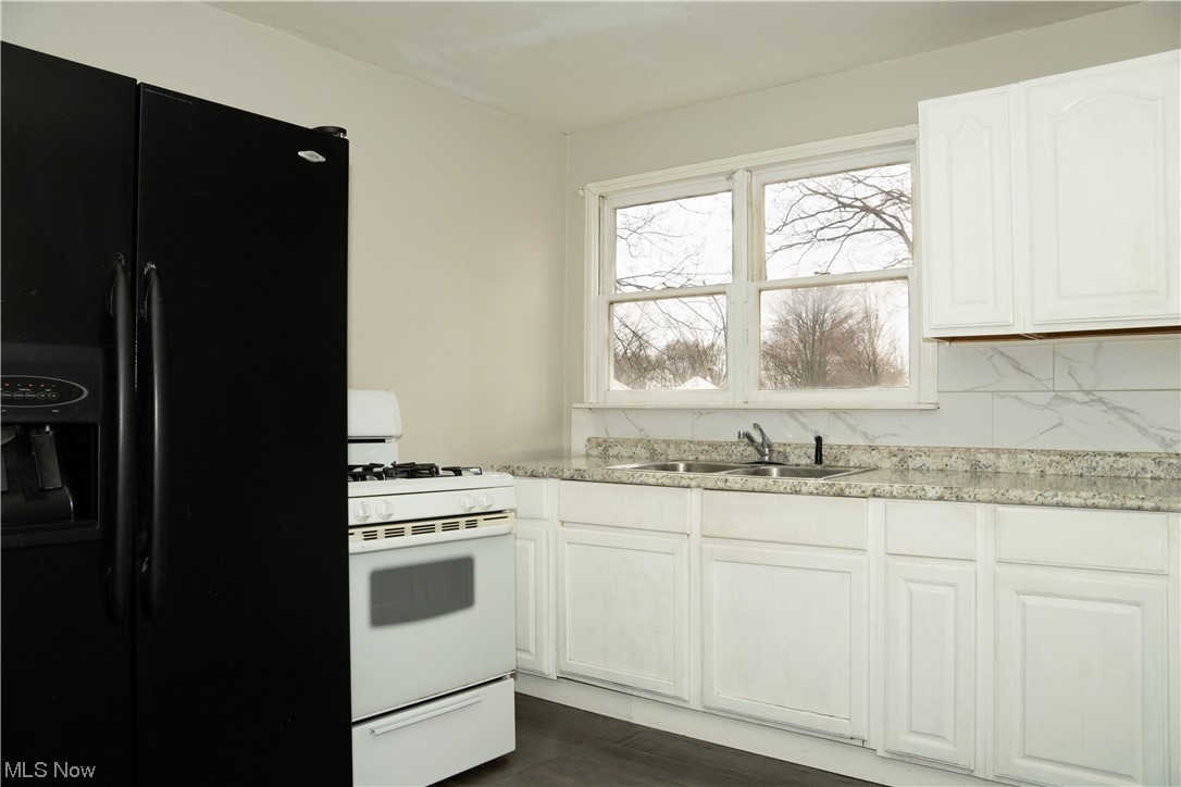 32 Lee Road Painesville, OH 44077 - Photo 3 of 12 Kitchen with light stone countertops, gas range gas stove, black fridge with ice dispenser, and white cabinets