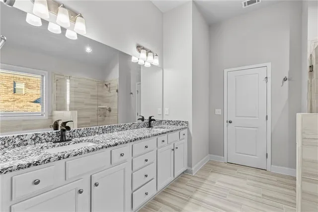 a bathroom with a granite countertop double vanity sink a mirror and a shower