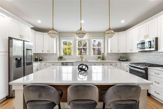 a kitchen with stainless steel appliances granite countertop a sink a stove a refrigerator cabinets and chairs