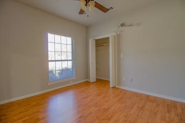 an empty room with wooden floor fan and windows