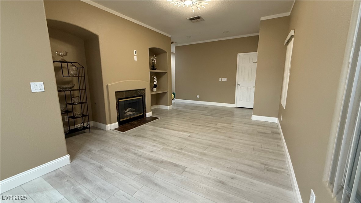 7062 Russell Ranch Avenue Las Vegas, NV 89113 - Photo 11 of 32 Unfurnished living room featuring crown molding, a fireplace with flush hearth, arched walkways, visible vents, and built in shelves