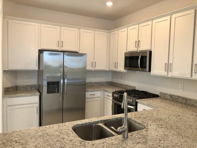 a kitchen with stainless steel appliances granite countertop a refrigerator a stove and a sink with wooden cabinets