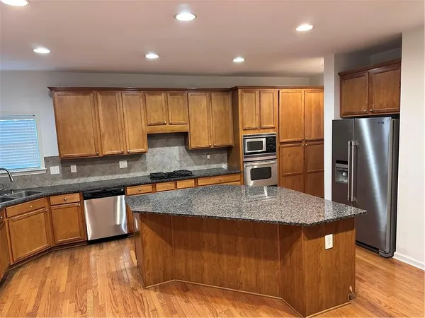 a kitchen with stainless steel appliances granite countertop a refrigerator a stove a sink and dishwasher wooden cabinets with wooden floor