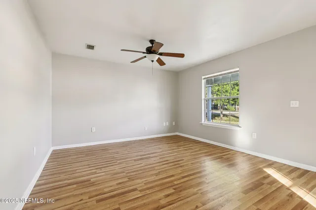 an empty room with wooden floor ceiling fan and windows