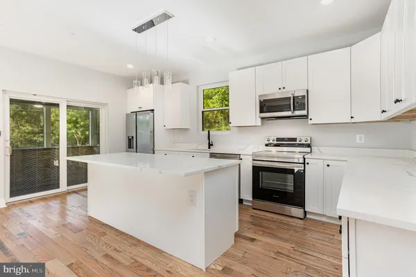 a kitchen with stainless steel appliances a stove top oven a sink a refrigerator white cabinets and wooden floor