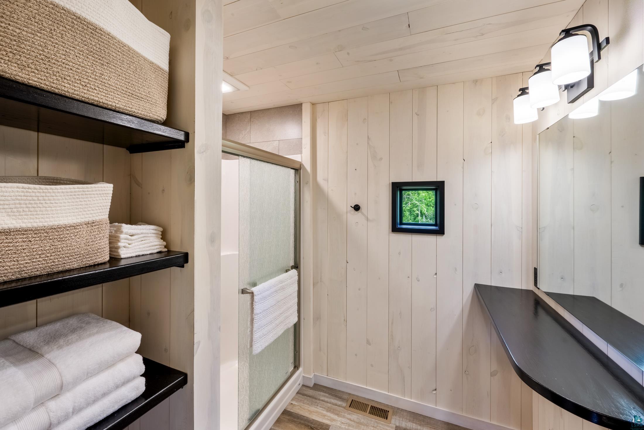 3778 East County Road Barnum, MN 55707 - Photo 39 of 52 Shiplap walls and ceiling, walk-in shower with frosted glass, built-in shelving, black vanity countertop, and vanity light fixture