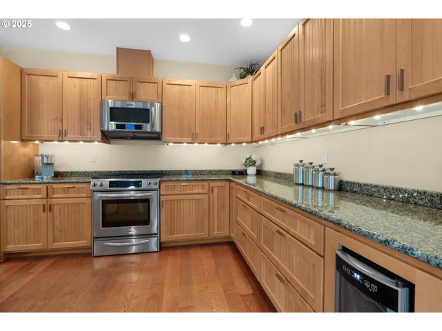 a kitchen with stainless steel appliances granite countertop a stove top oven a sink a dining table with wooden floor