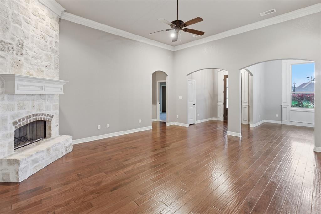 7765 Hickory Spring Lane Tyler, TX 75703 - Photo 13 of 38 Spacious living area featuring a stone-clad fireplace with mantel, hardwood flooring, arched doorways, crown molding, and a ceiling fan