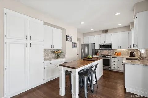 a kitchen with stainless steel appliances a stove a sink a refrigerator and white cabinets with wooden floor
