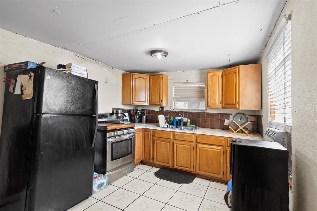 7826 Rilla Avenue Dallas, TX 75217 - Photo 5 of 10 Kitchen featuring freestanding refrigerator, brown cabinetry, gas stove, light tile patterned flooring, and range