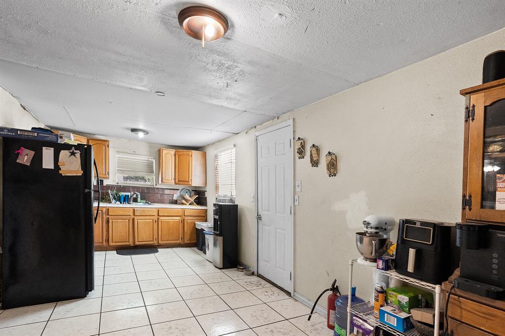 7826 Rilla Avenue Dallas, TX 75217 - Photo 6 of 10 Kitchen with freestanding refrigerator, light tile patterned flooring, light countertops, a textured ceiling, and brown cabinets