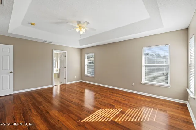 an empty room with wooden floor chandelier and windows