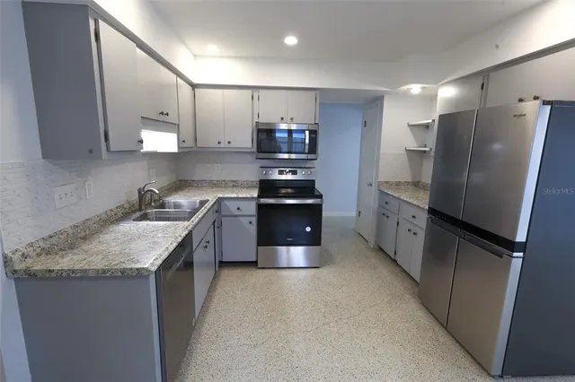 a kitchen with stainless steel appliances granite countertop a refrigerator a sink a stove and a refrigerator with wooden floor