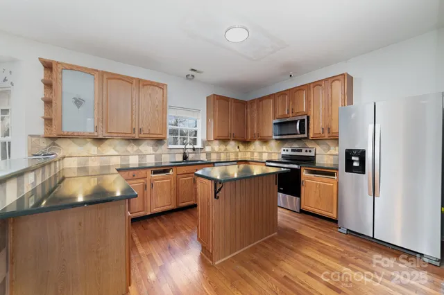 a kitchen with stainless steel appliances granite countertop a refrigerator a sink dishwasher a stove top oven a kitchen island and cabinets with wooden floor