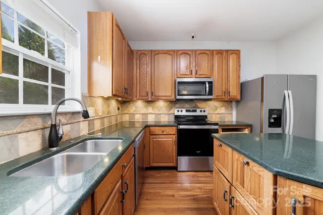 a kitchen with stainless steel appliances granite countertop a sink a stove top oven a refrigerator cabinets and a kitchen island