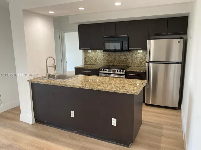 a kitchen with kitchen island stainless steel appliances granite countertop a refrigerator a sink and a stove