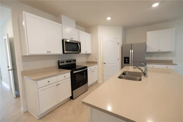 a large white kitchen with a sink a microwave a stove and refrigerator