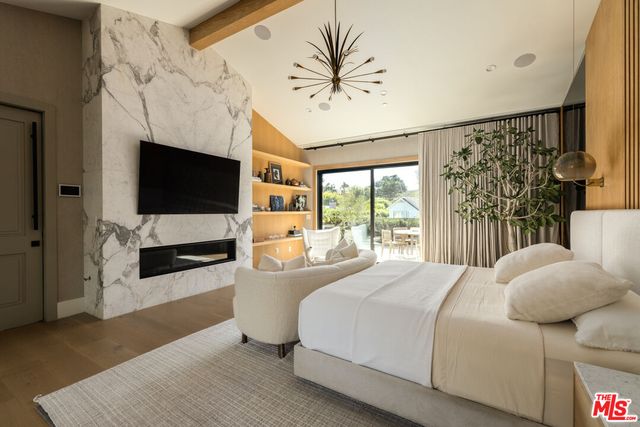 a bedroom with a large bed a flat tv screen and a fireplace with wooden floor