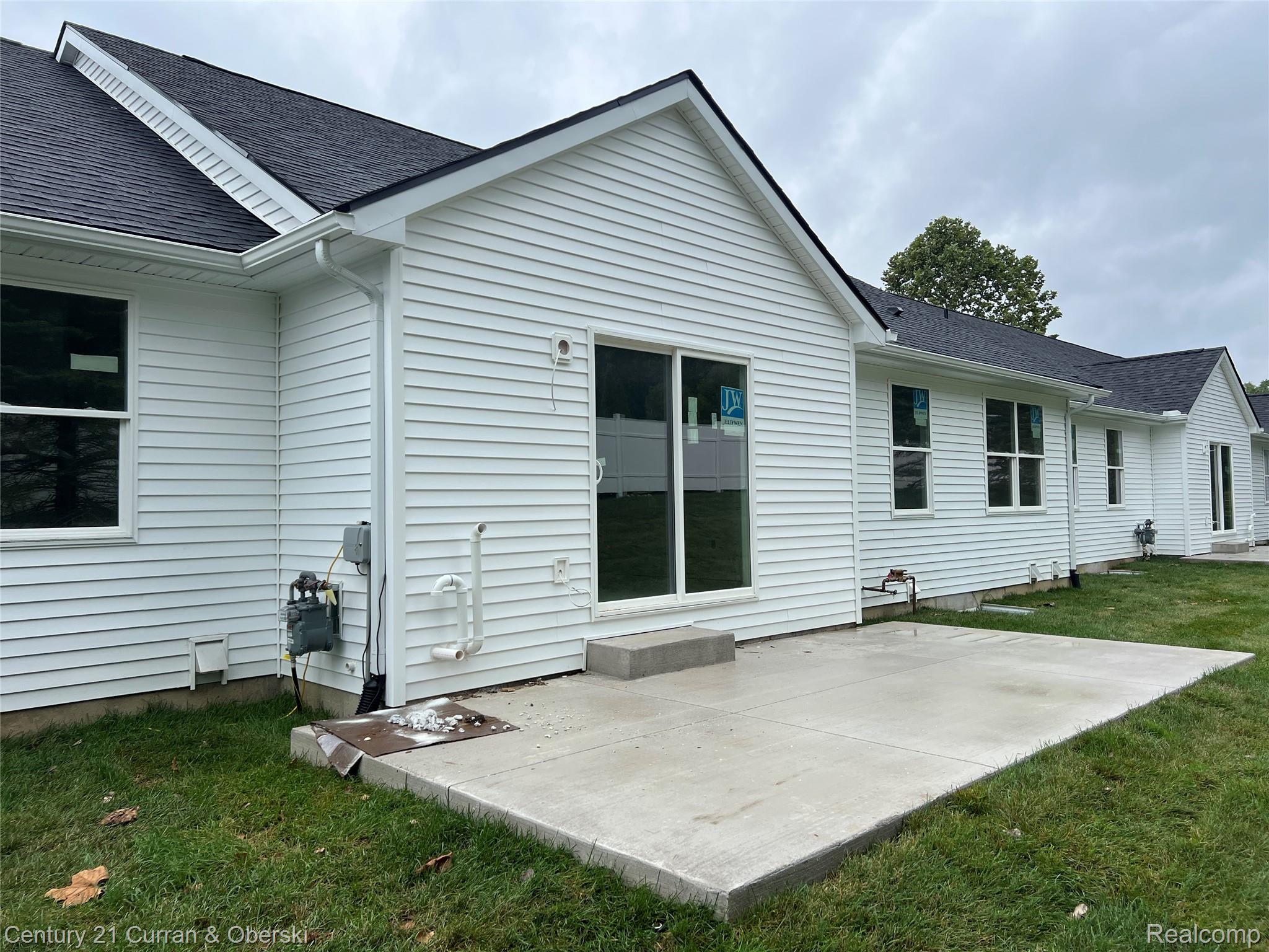 821 Nelson's Ridge Drive, Unit 12 Howell, MI 48843 - Photo 2 of 2 Exterior featuring white horizontal siding, a dark shingle roof, multiple windows, a sliding glass door, and a concrete patio