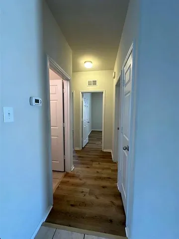 a view of a hallway with wooden floor and a bathroom