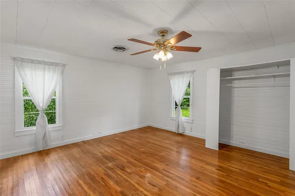 an empty room with wooden floor chandelier fan and windows