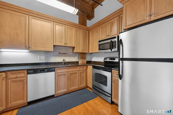a kitchen with stainless steel appliances granite countertop a refrigerator a sink dishwasher and white cabinets with wooden floor