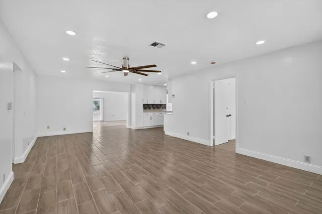 an empty room with wooden floor kitchen view and windows