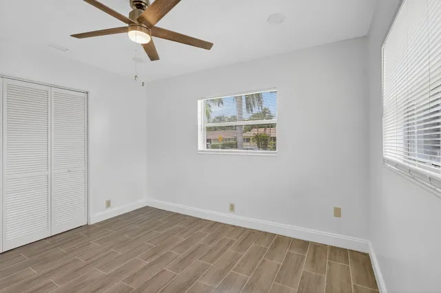 an empty room with wooden floor ceiling fan and window