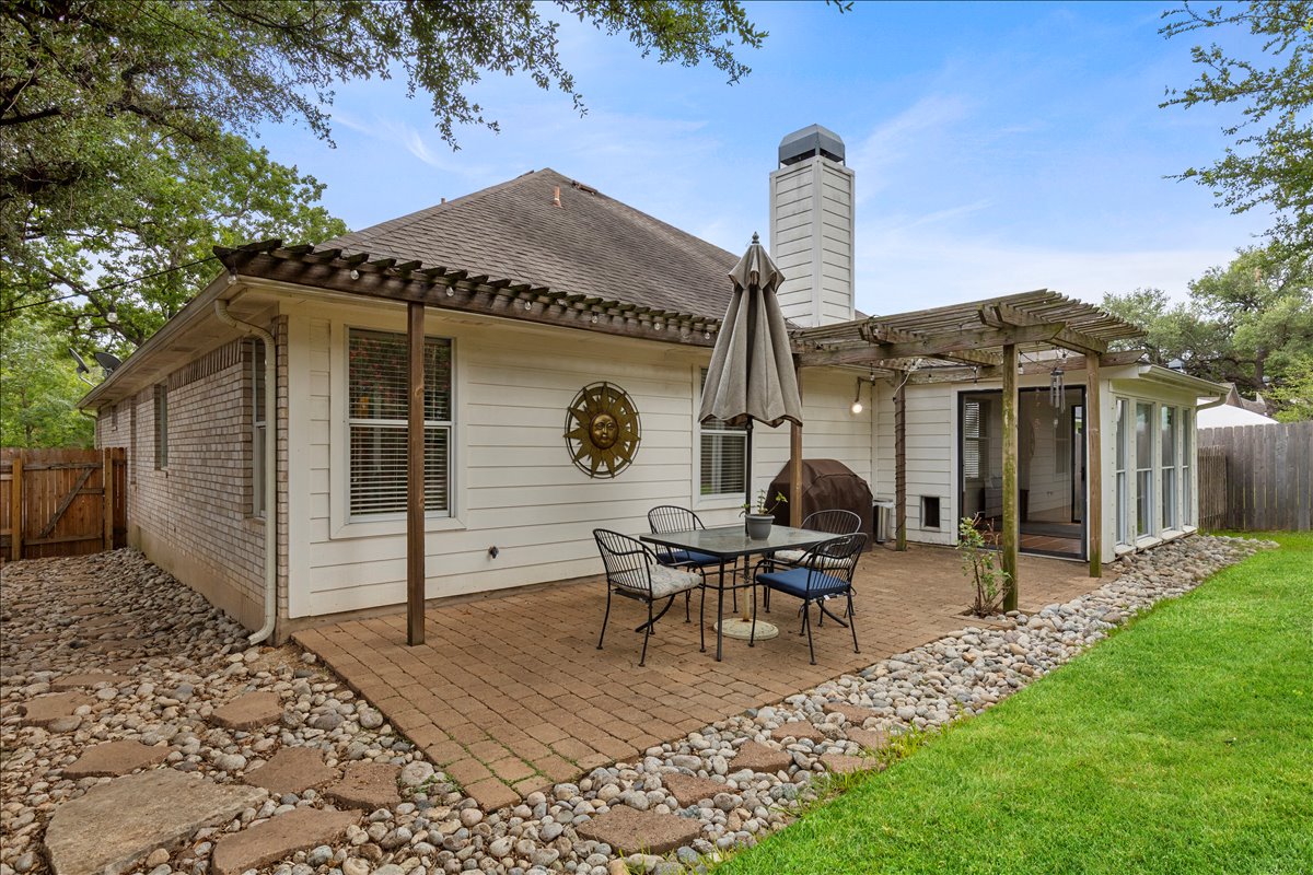 9012 Meacham Way Austin, TX 78749 - Photo 28 of 34 Expansive backyard featuring a paver patio with a wood pergola, green lawn, stone-lined landscaping beds, and a sunroom with large windows