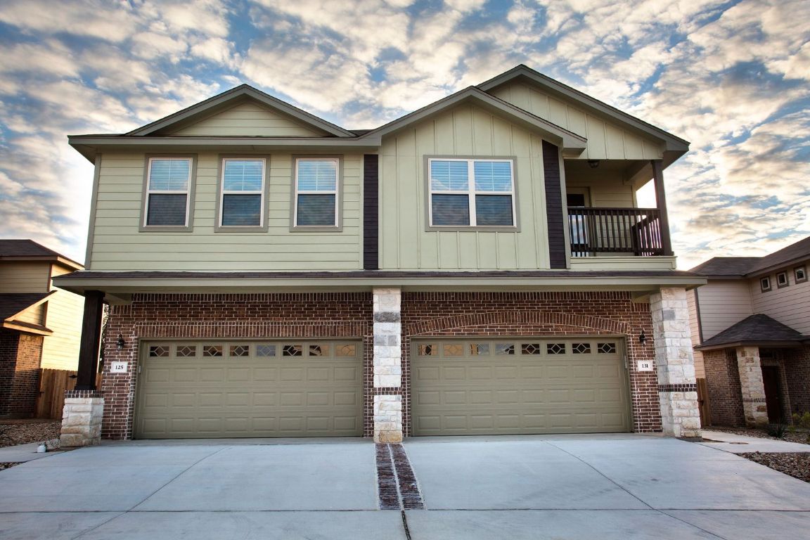 View of front of home with a balcony, driveway, a garage, board and batten siding, and brick siding