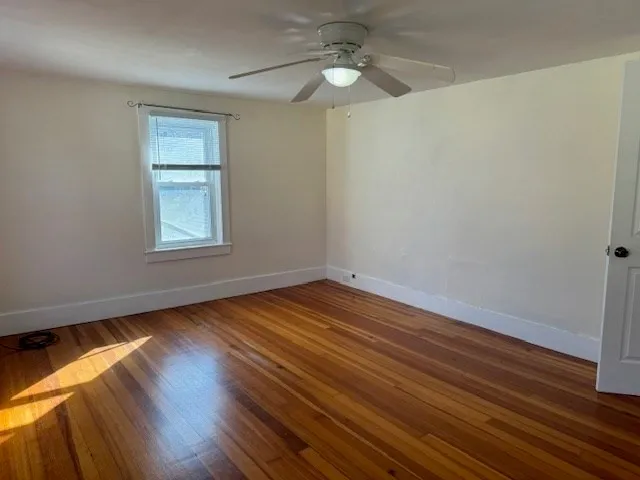 an empty room with wooden floor chandelier fan and windows