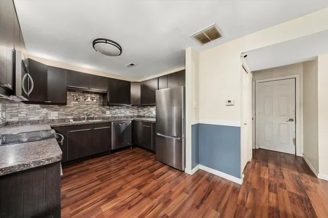 a kitchen with stainless steel appliances kitchen island granite countertop a refrigerator a sink dishwasher a stove and white countertops with wooden floor